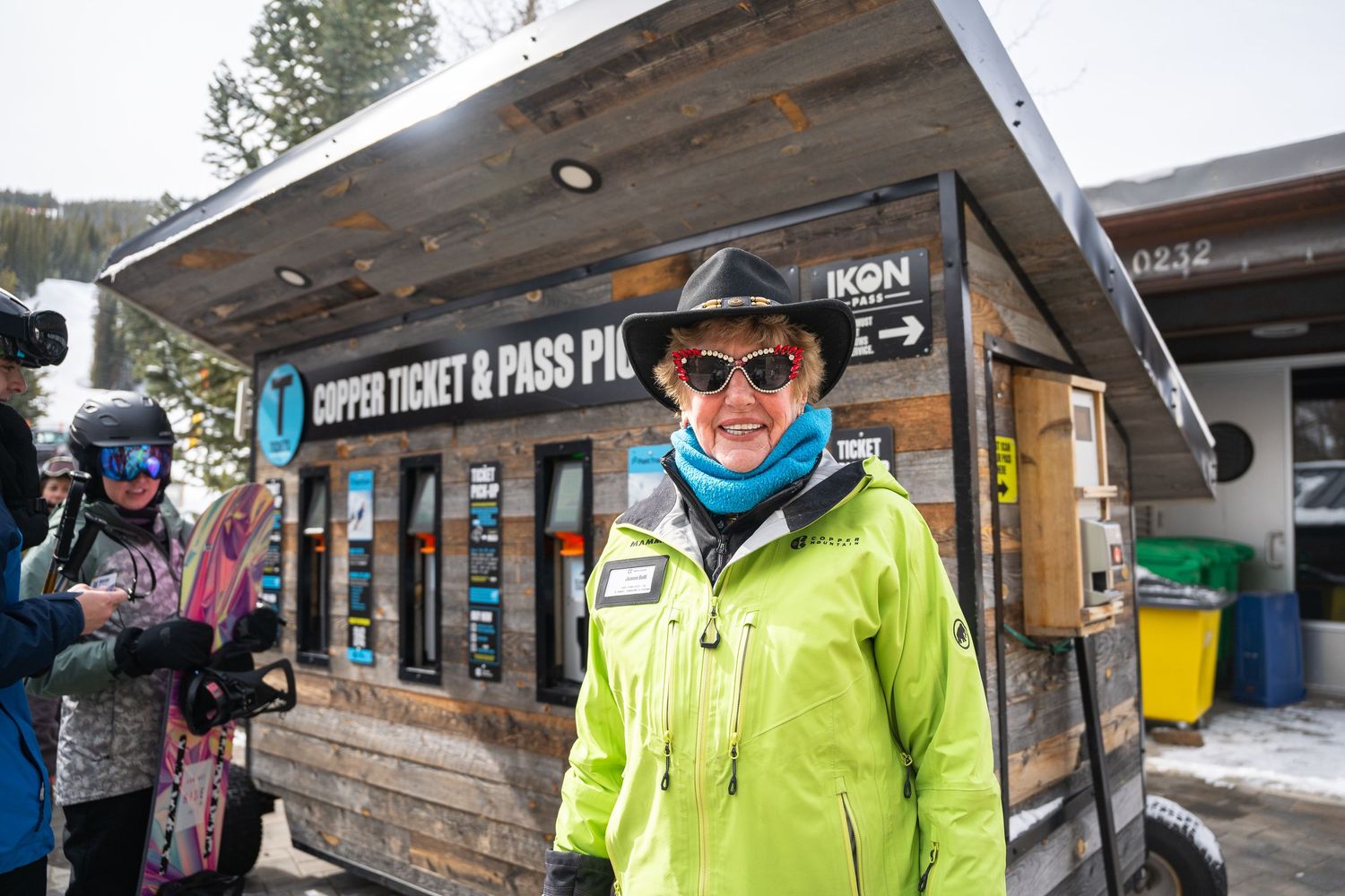 Ski resort employee in bright yellow jacket stands in front of ticket window during winter.