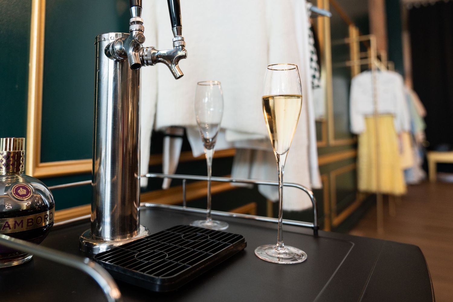 Two champagne flutes filled with sparkling wine beside a silver beer tap on a dark counter in an elegant bar setting.