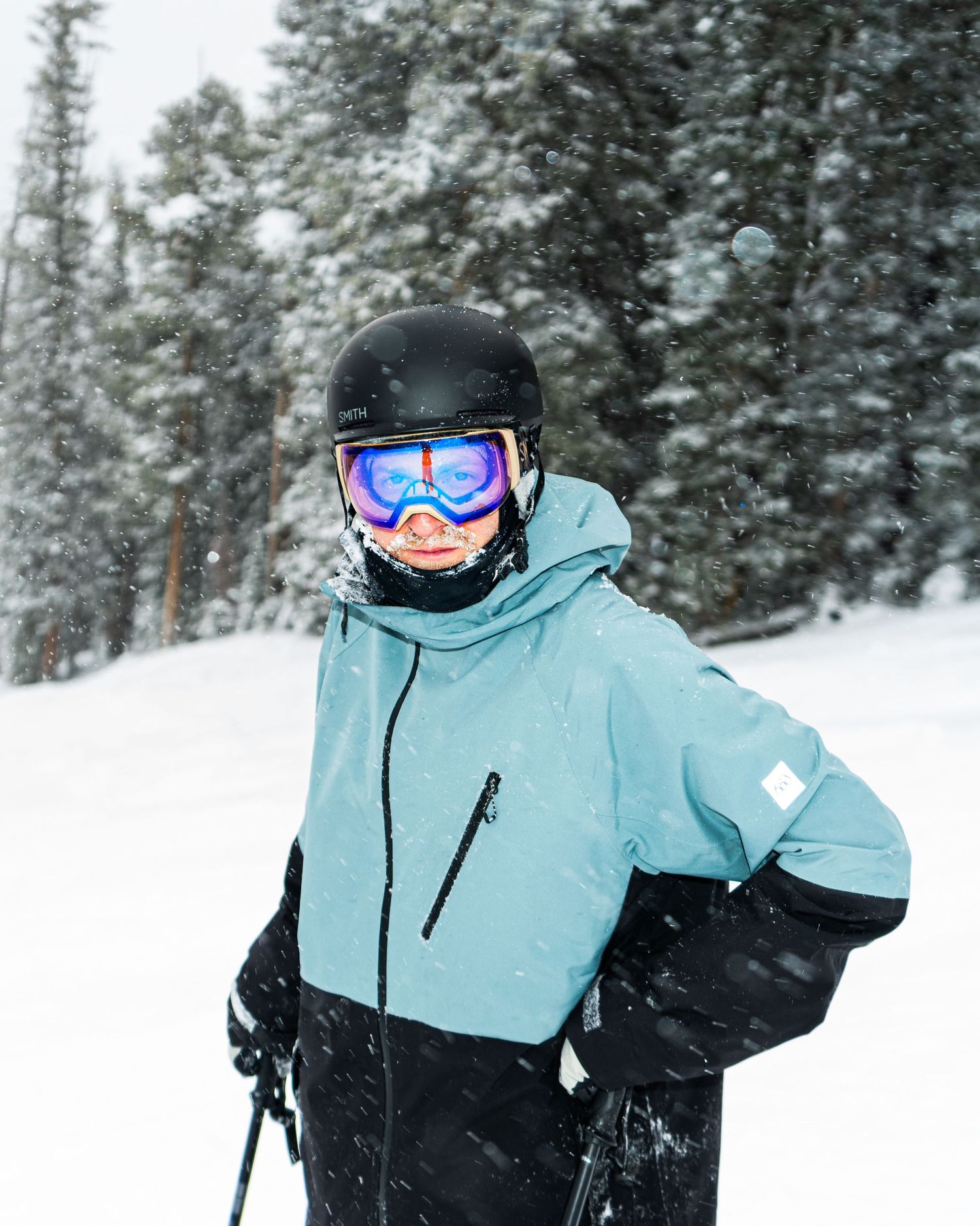 Winter sports enthusiast in light blue jacket and ski helmet against snowy forest backdrop.