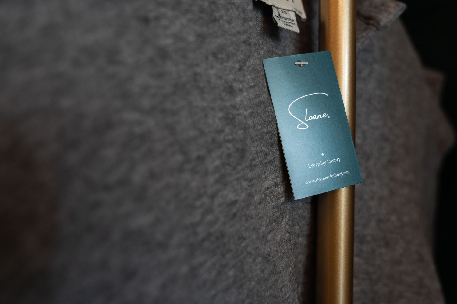 Row of sleek golden and black designer clothing hangers with branded tags mounted against a dark background.