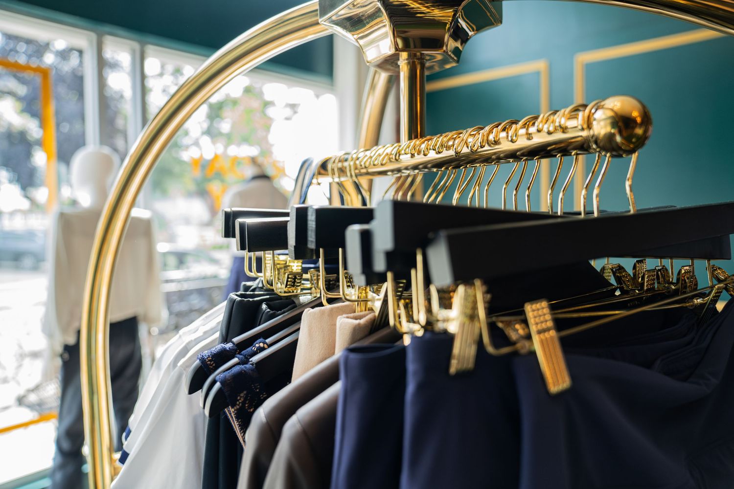 Gold clothing rack with navy, white, and gray garments hanging in a boutique store with teal walls.