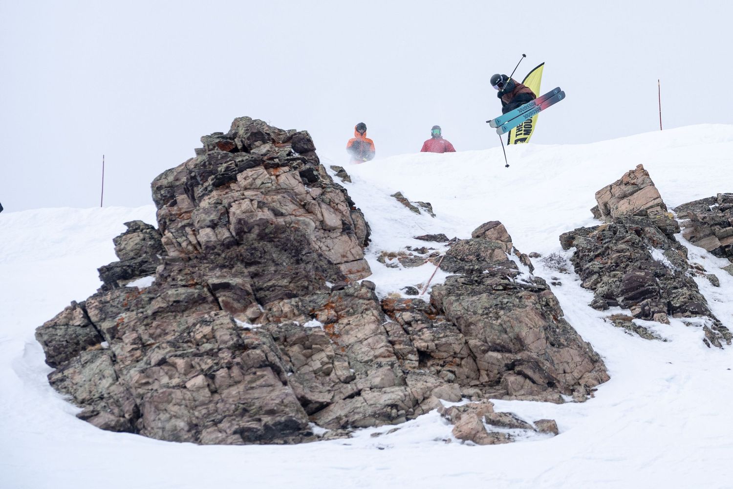 Skier performs aerial jump over rocky outcrop in snowy terrain.