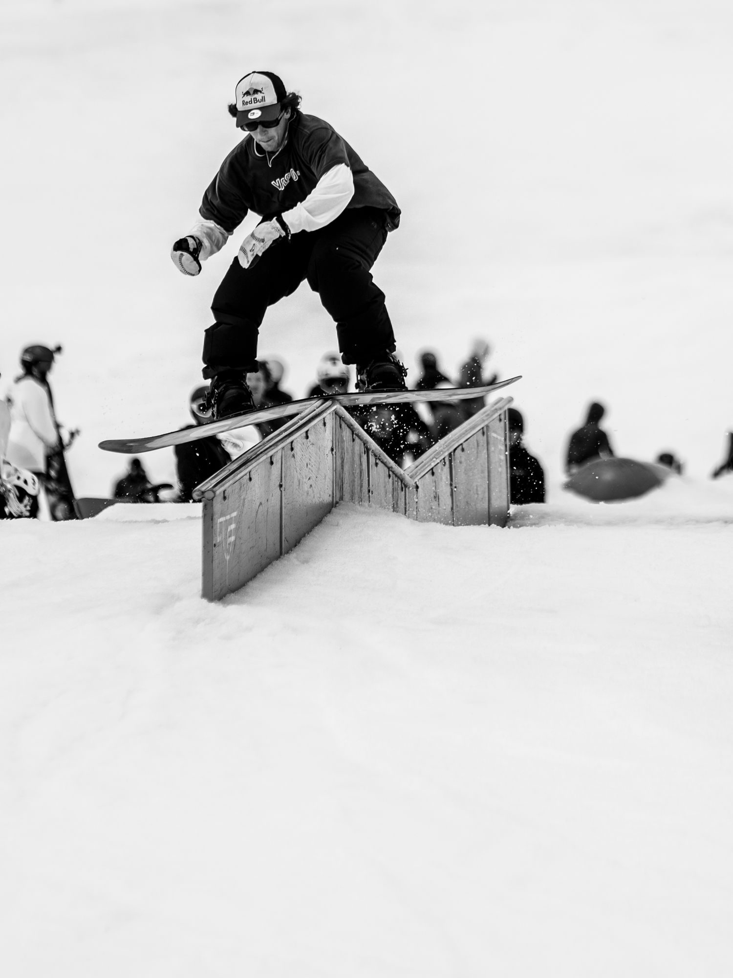 Monochrome photo of a snowboarder jumping on a rail in a terrain park.