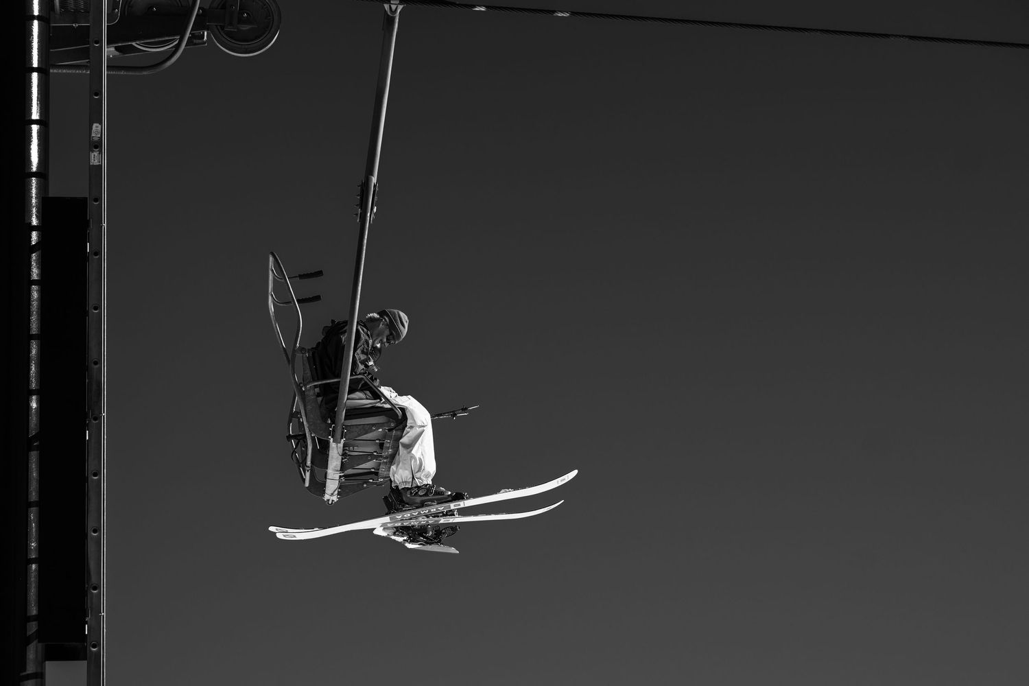 Black and white silhouette of person riding chairlift against dark sky.
