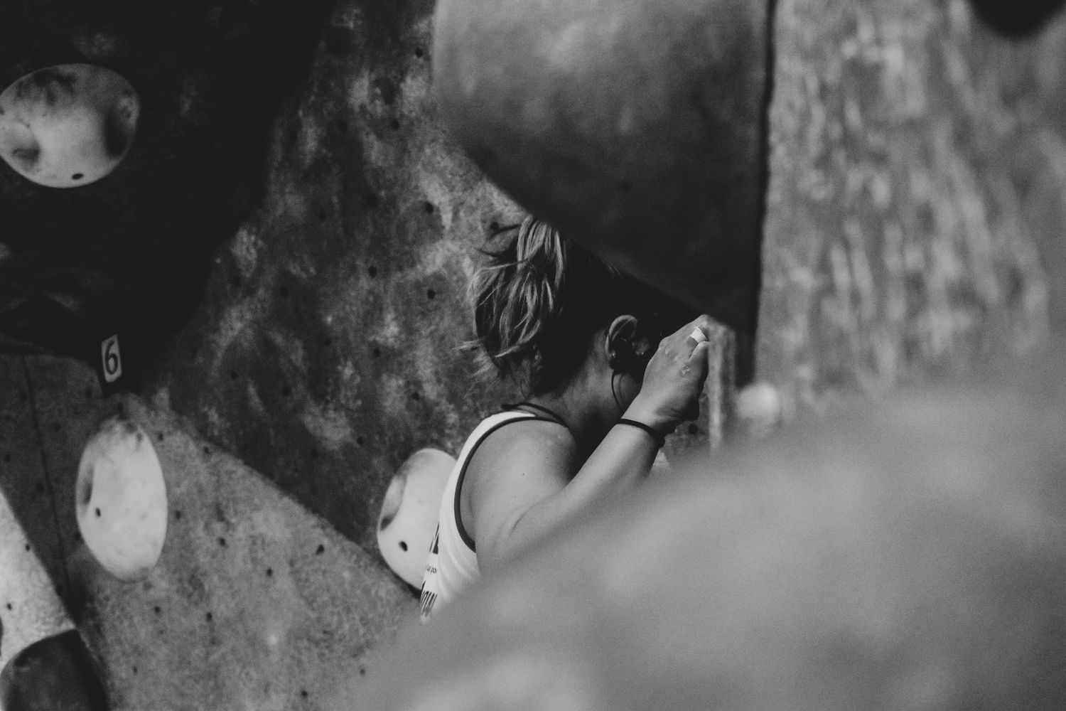 Monochrome close-up shot of a rock climber gripping holds on an indoor climbing wall.