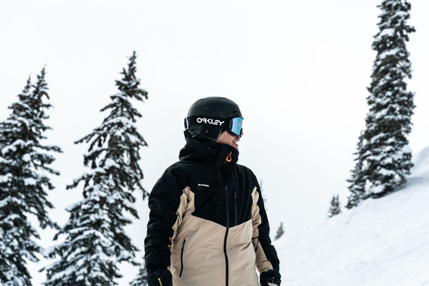 Winter sports enthusiast in black and tan jacket standing on snowy mountain slope.
