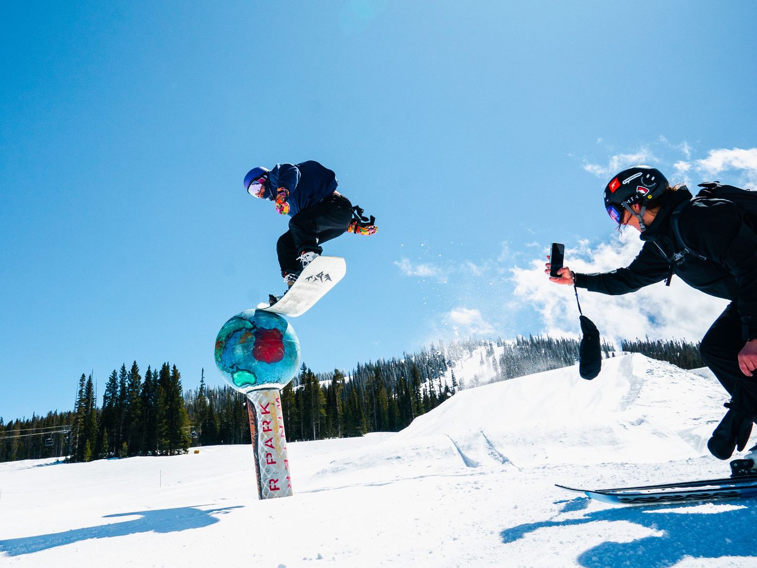 Two snowboarders performing aerial tricks over snow park jump.