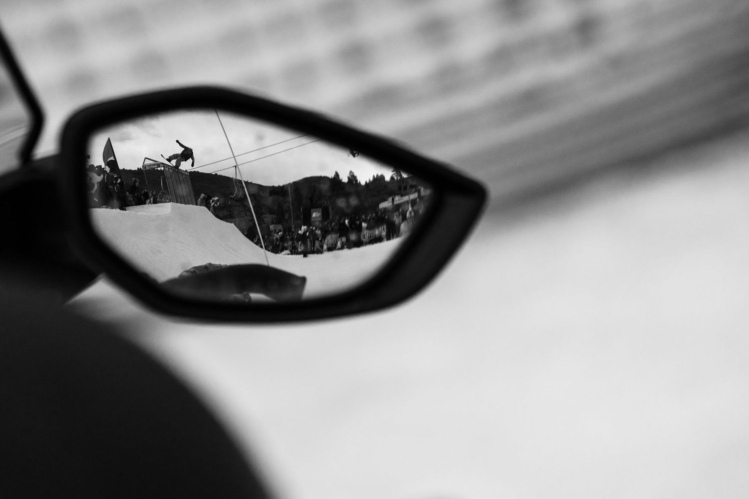 Black and white reflection of a BMX rider performing a trick captured in a car side mirror.