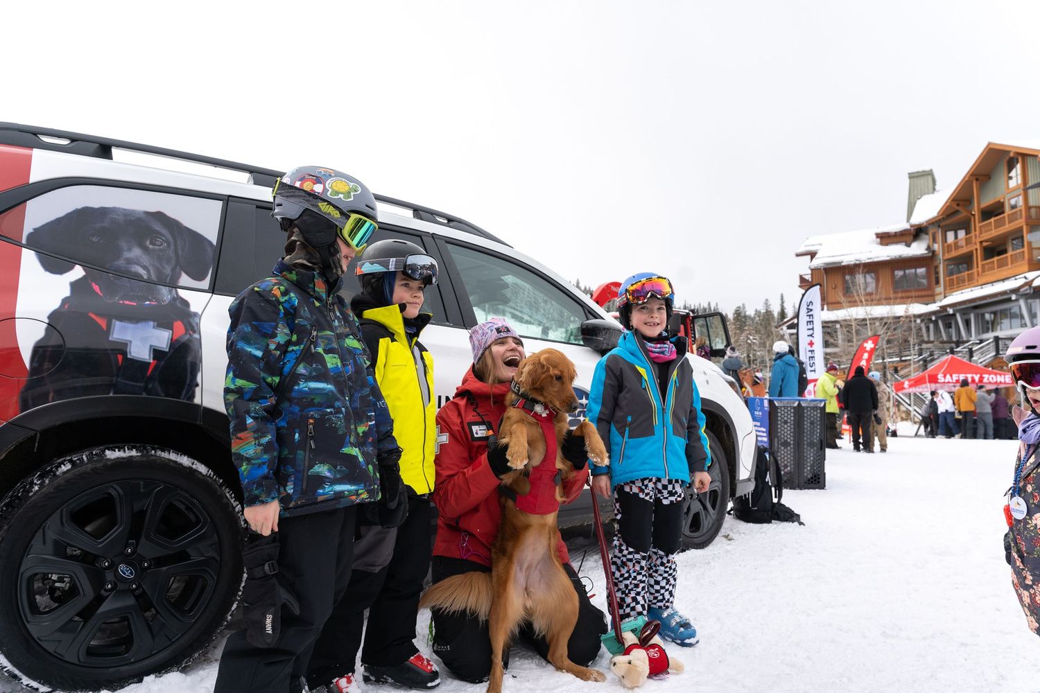 Group of winter sports enthusiasts and a dog posing by their vehicle in snowy conditions.
