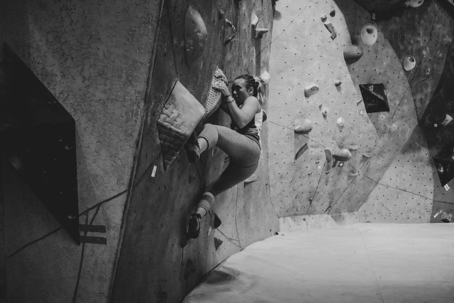 Sport climber navigates challenging route on indoor climbing wall in monochrome.
