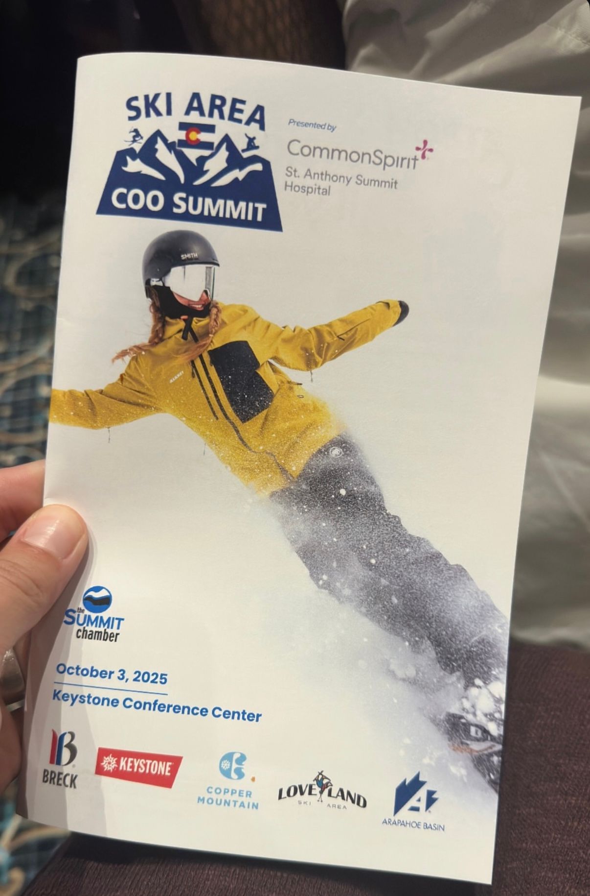 A ski event promotional material showing a skier in yellow jacket performing a jump against a white snowy background.