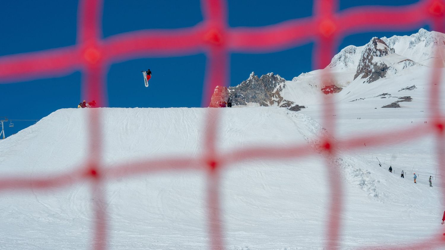 Snow-covered mountain peak viewed through red safety netting.