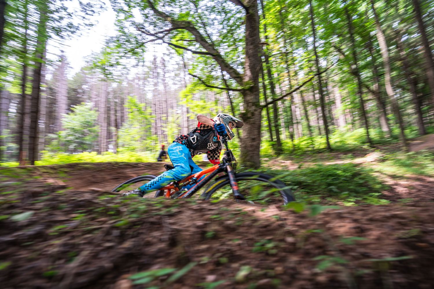Mountain biker rides through lush green forest terrain during summertime action sports adventure.
