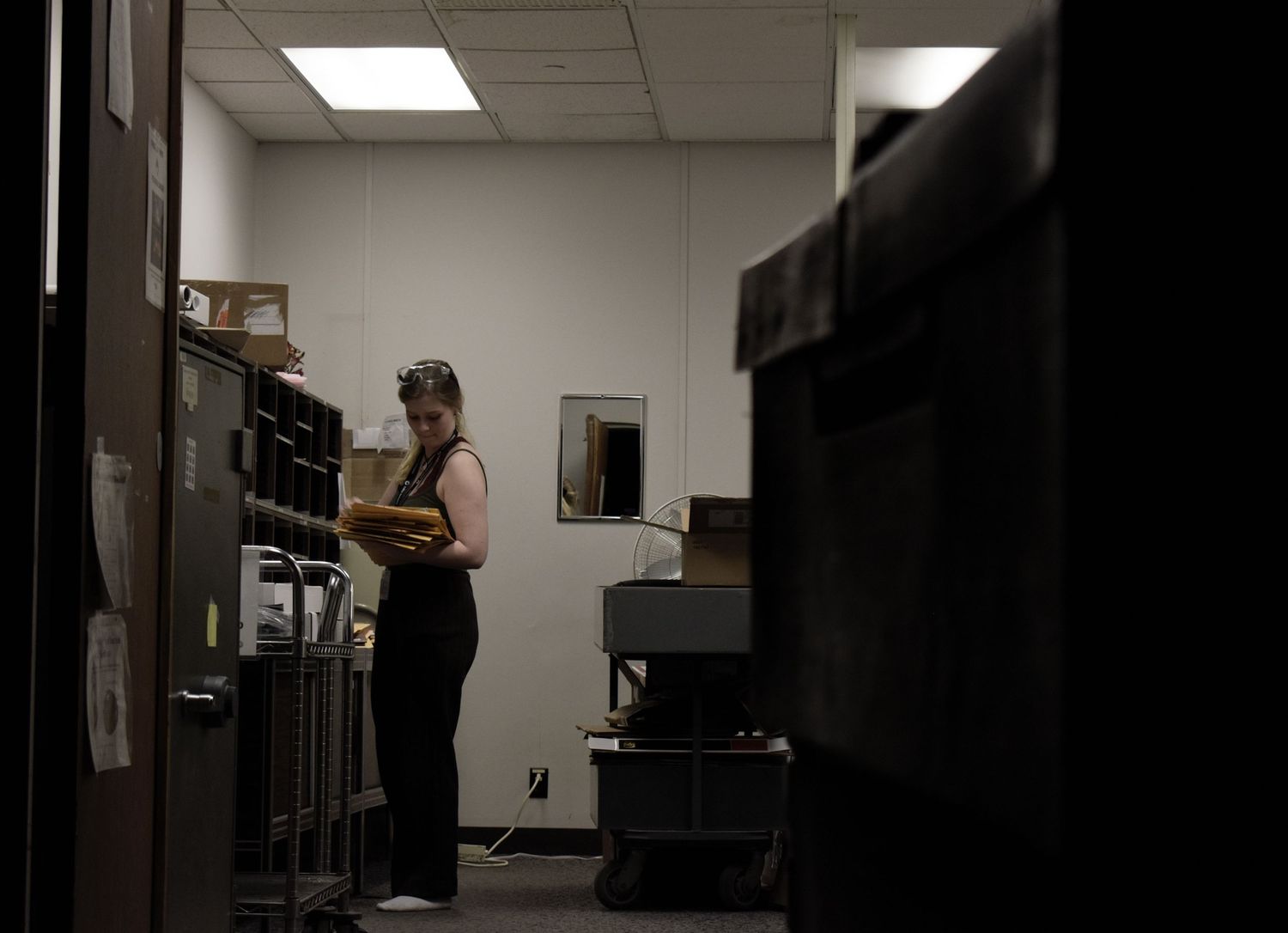 A dimly lit office or storage room with electronic equipment and shelving visible in the shadowy space.
