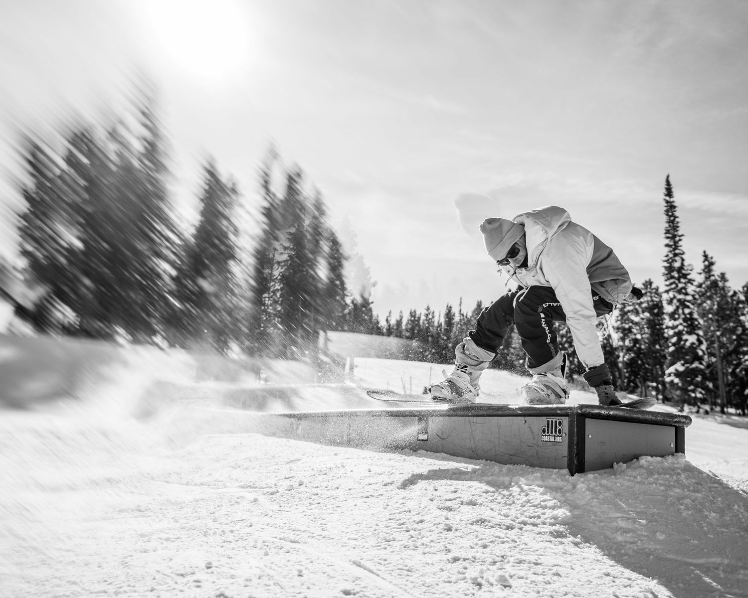 Black and white photo of snowboarder performing trick on terrain park box feature.