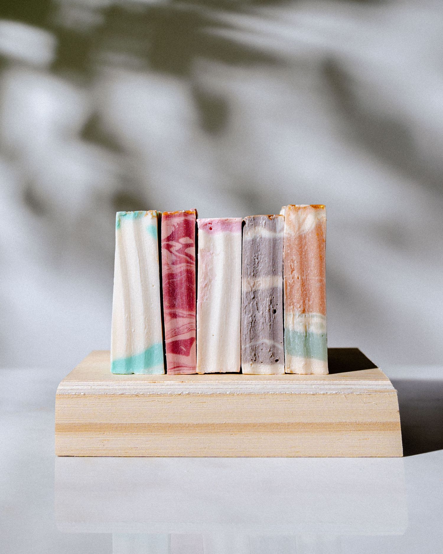 A sequence of soap bars in various shades of pink and white arranged in a minimalist composition on a light surface.