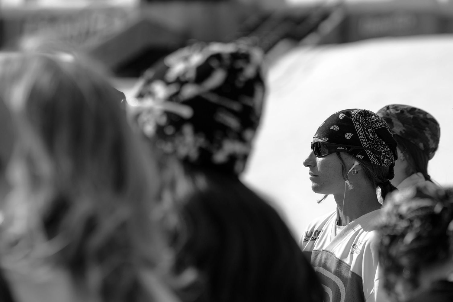 Black and white photo of a woman wearing a bandana and sunglasses standing in a crowd outdoors.