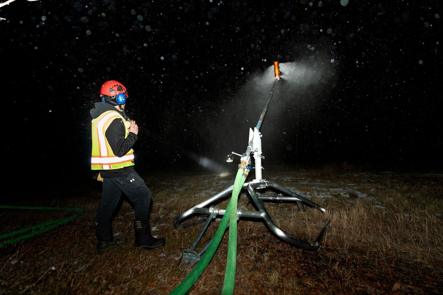 Worker operating snowmaking equipment at night with bright spotlights illuminating the snow.