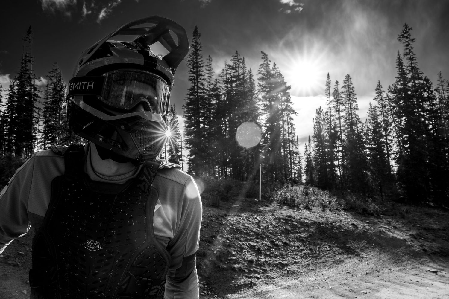 Dramatic backlit portrait of mountain biker in protective gear against forest backdrop.