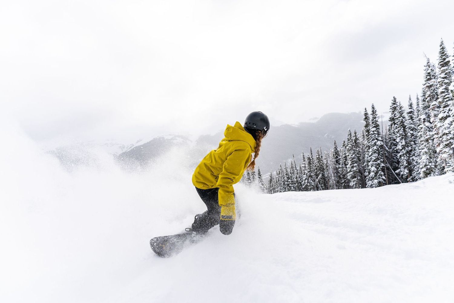 Snowboarder in yellow jacket carves through fresh powder on snowy mountain slope.