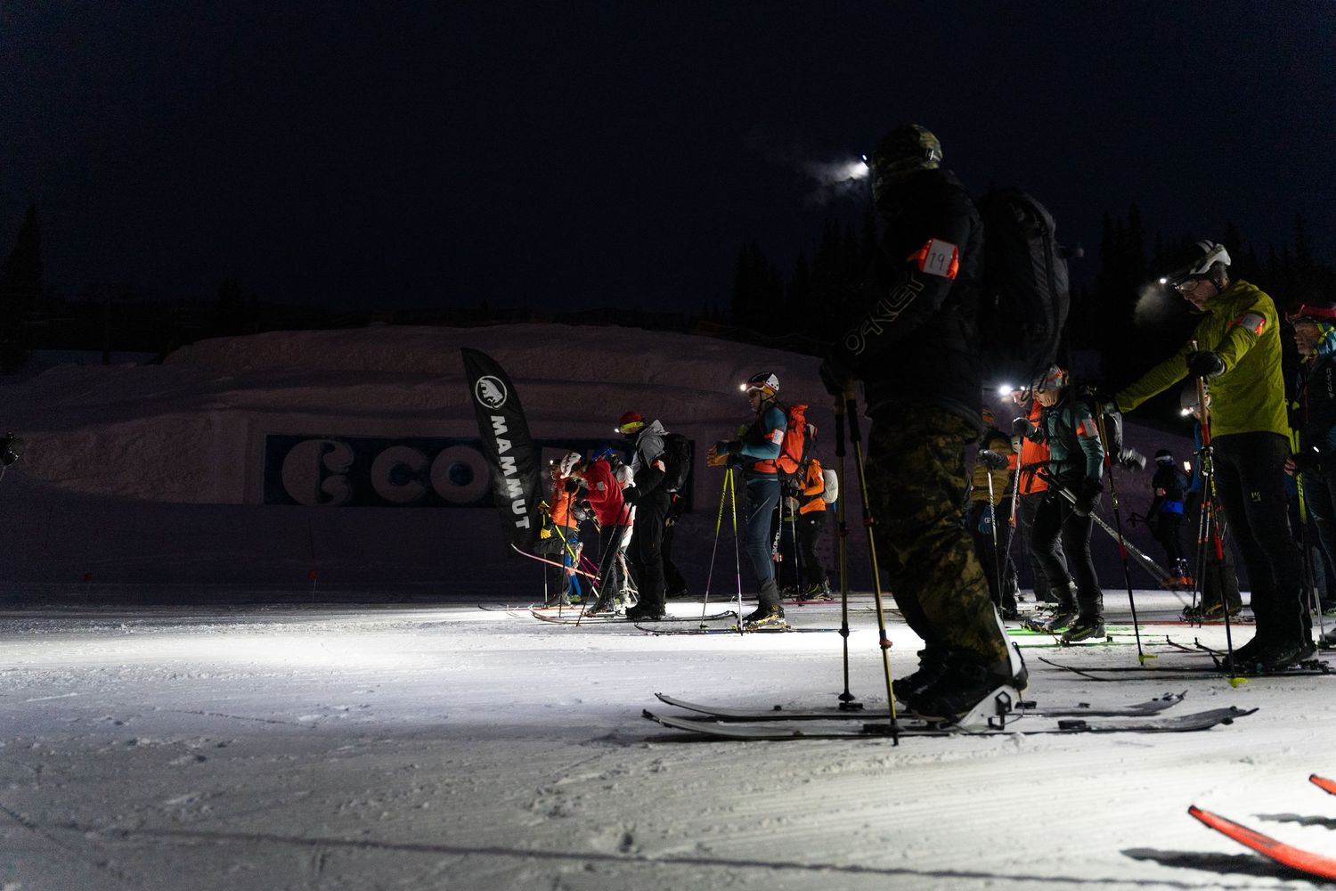 Night skiing group illuminated by headlamps on a dark snow-covered slope.