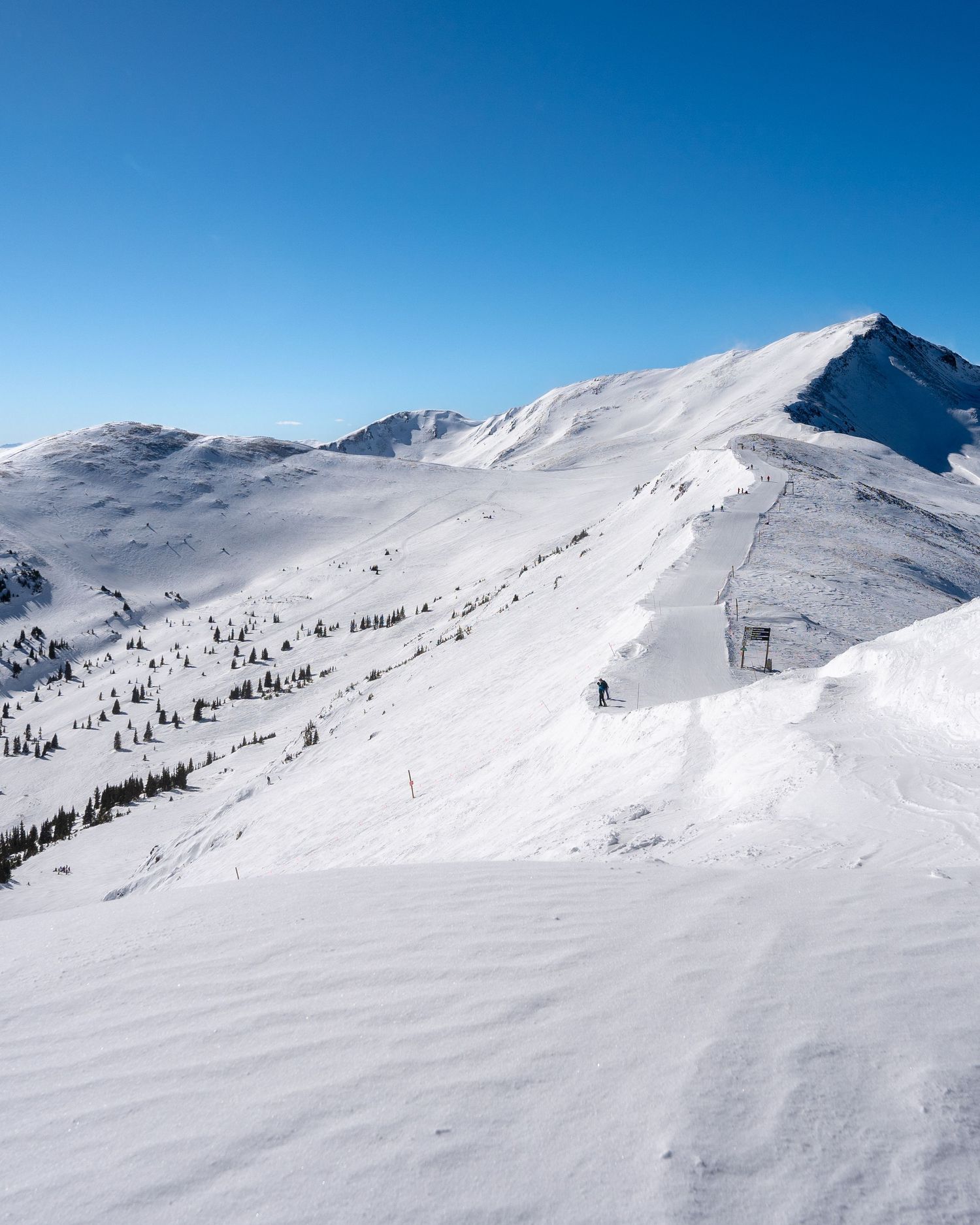 Panoramic view of ski resort with groomed slopes and lift infrastructure on snowy mountain.