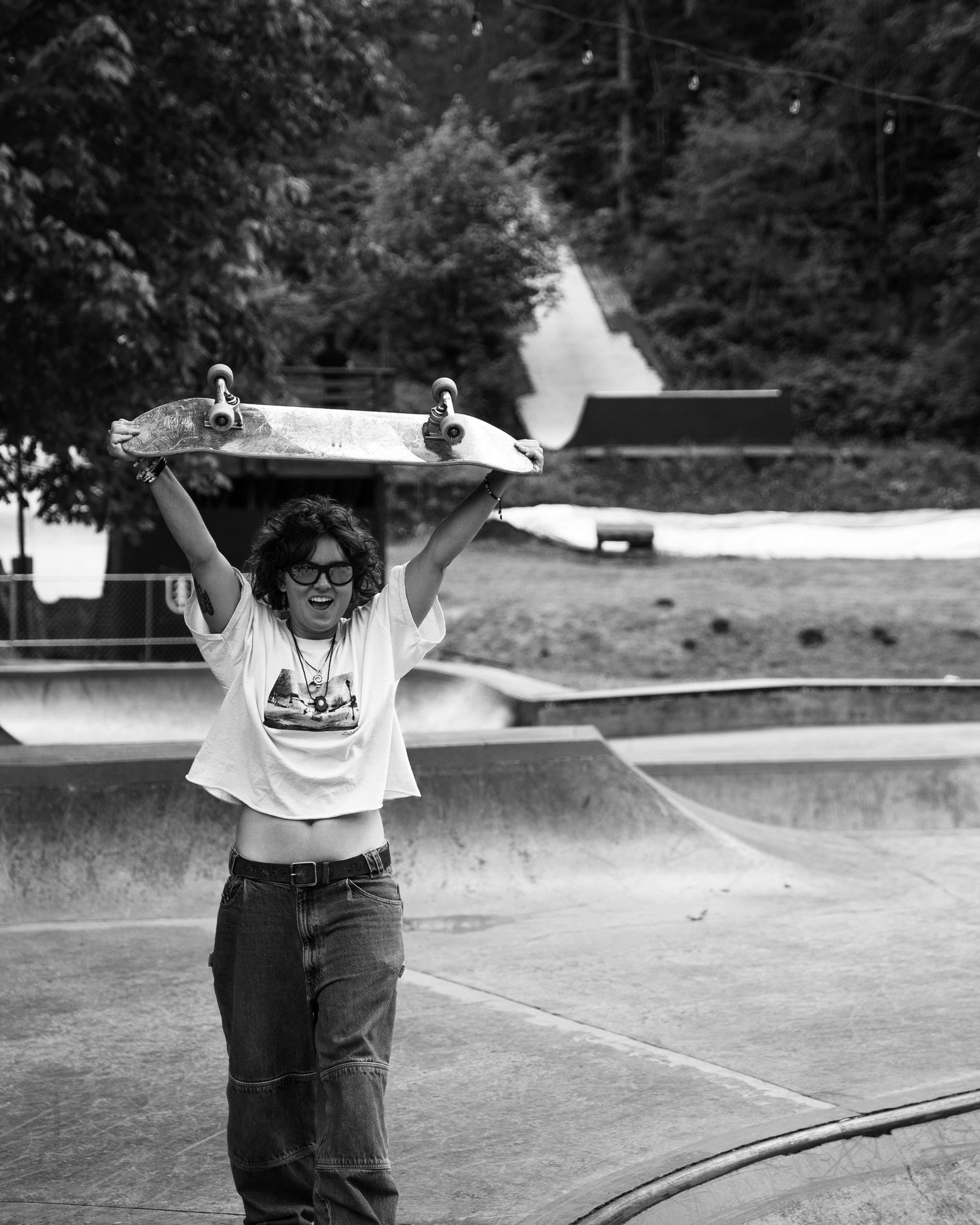 A skateboarder holding their board overhead at a skate park in vintage black and white photography.