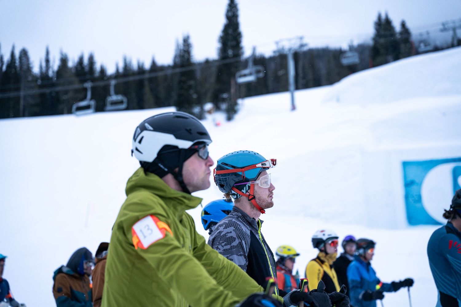 Skiers in bright gear stand together on snowy slopes with evergreen trees in background.