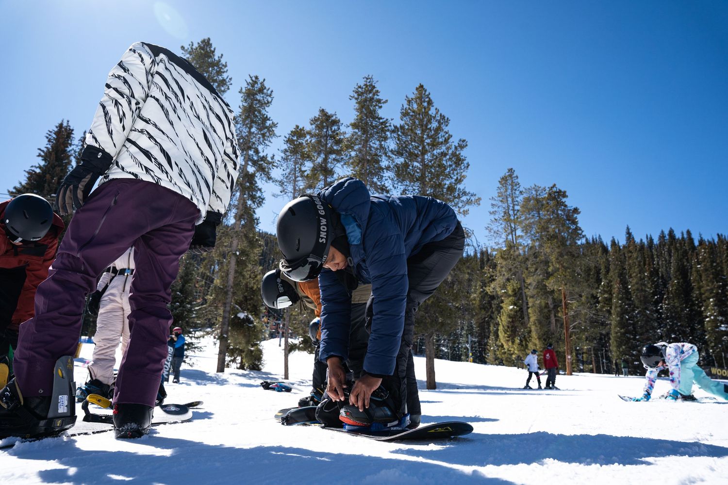Snowboarders bending down to adjust bindings on their snowboards in winter mountain setting.