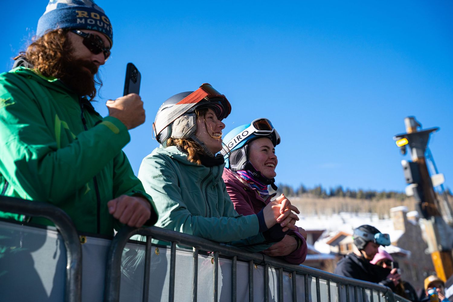 Spectators watching winter sports event from behind safety barrier on snowy slope.