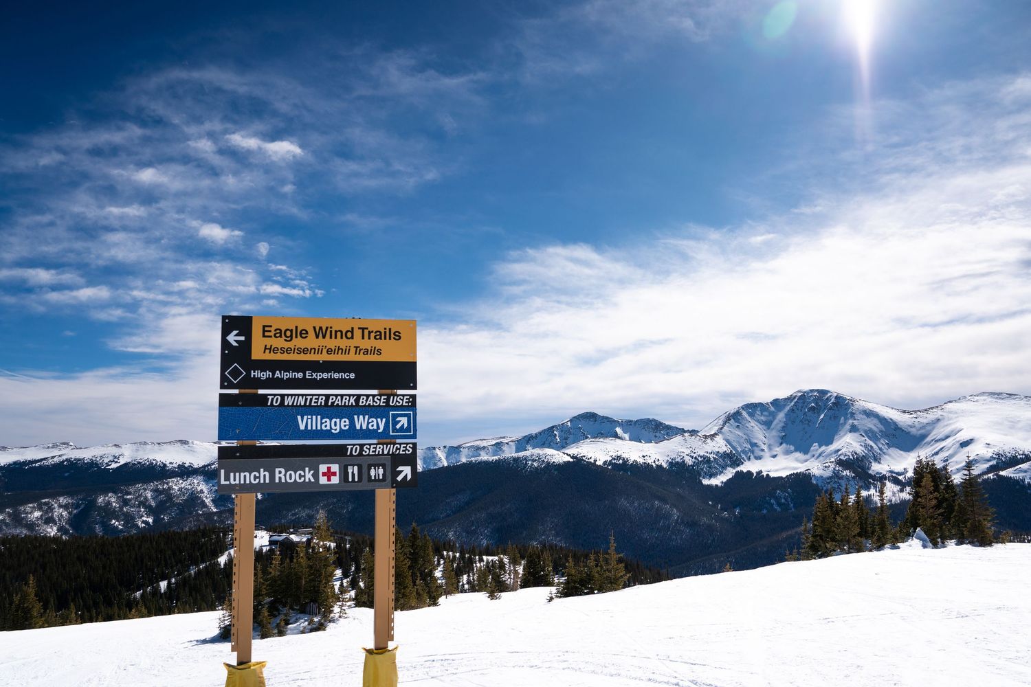 Mountain wayfinding sign for Eagle Wind Trails with snow-capped peaks in background.