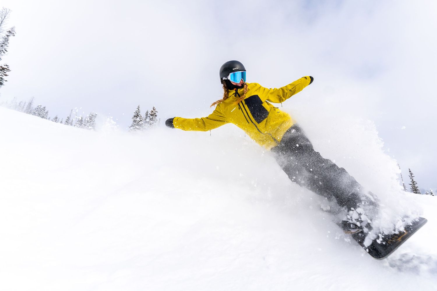 Snowboarder in yellow jacket catching air while riding through fresh powder snow.