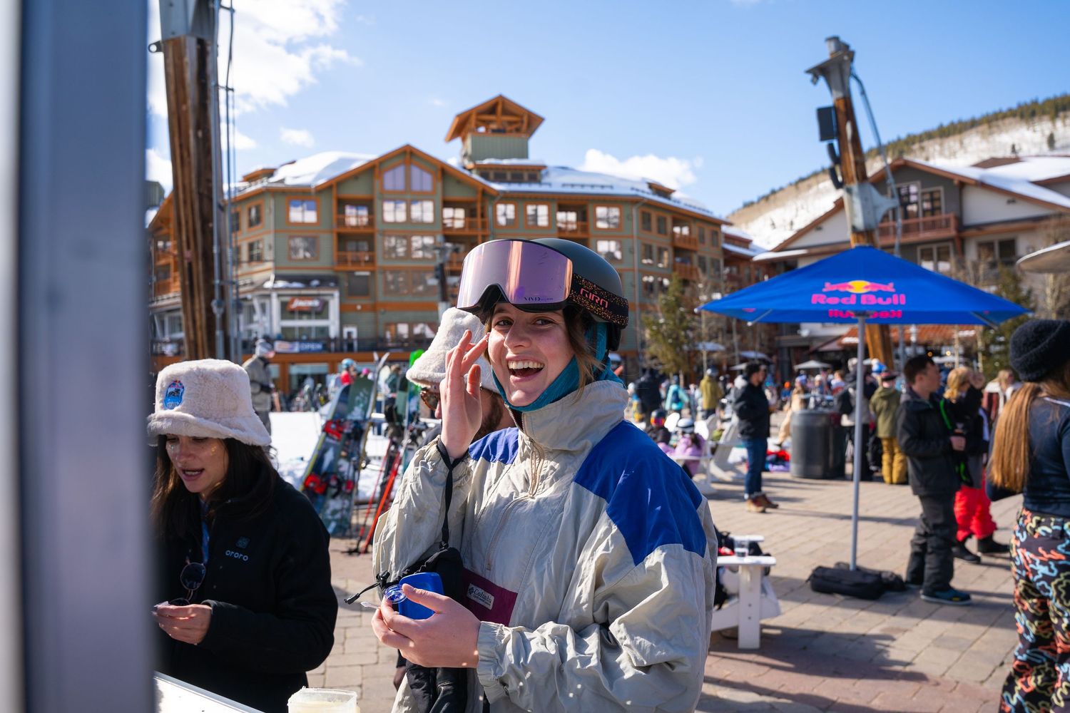 Skier enjoying refreshments at mountain resort base area on sunny day.