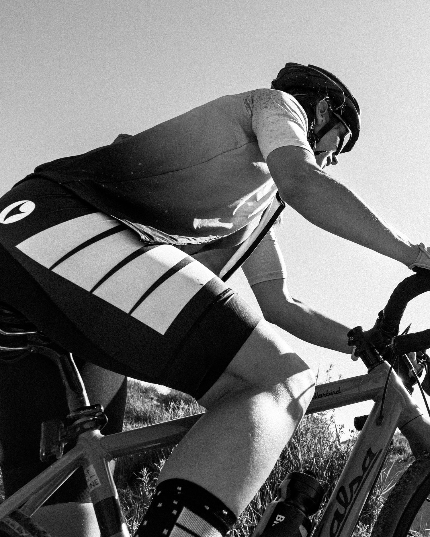 Black and white close-up of a cyclist in Pearl Izumi kit riding a road bike under a clear sky.