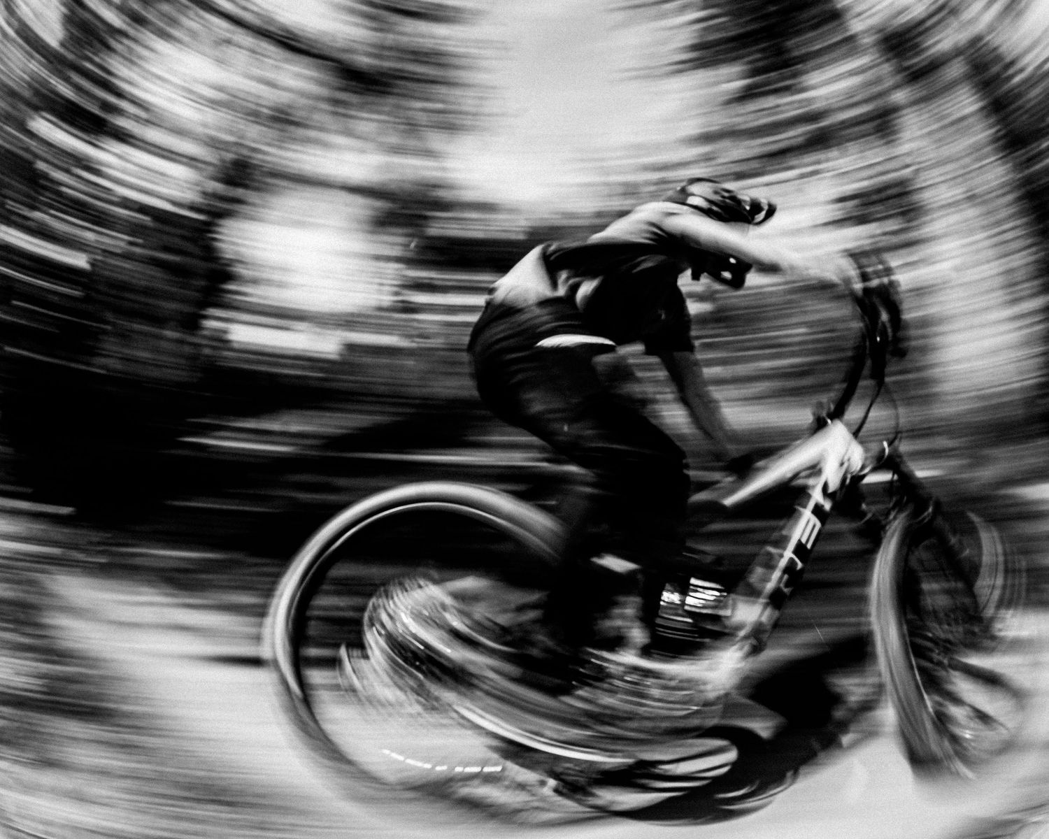 Black and white motion blur photograph of a mountain biker riding at high speed through a forest trail.