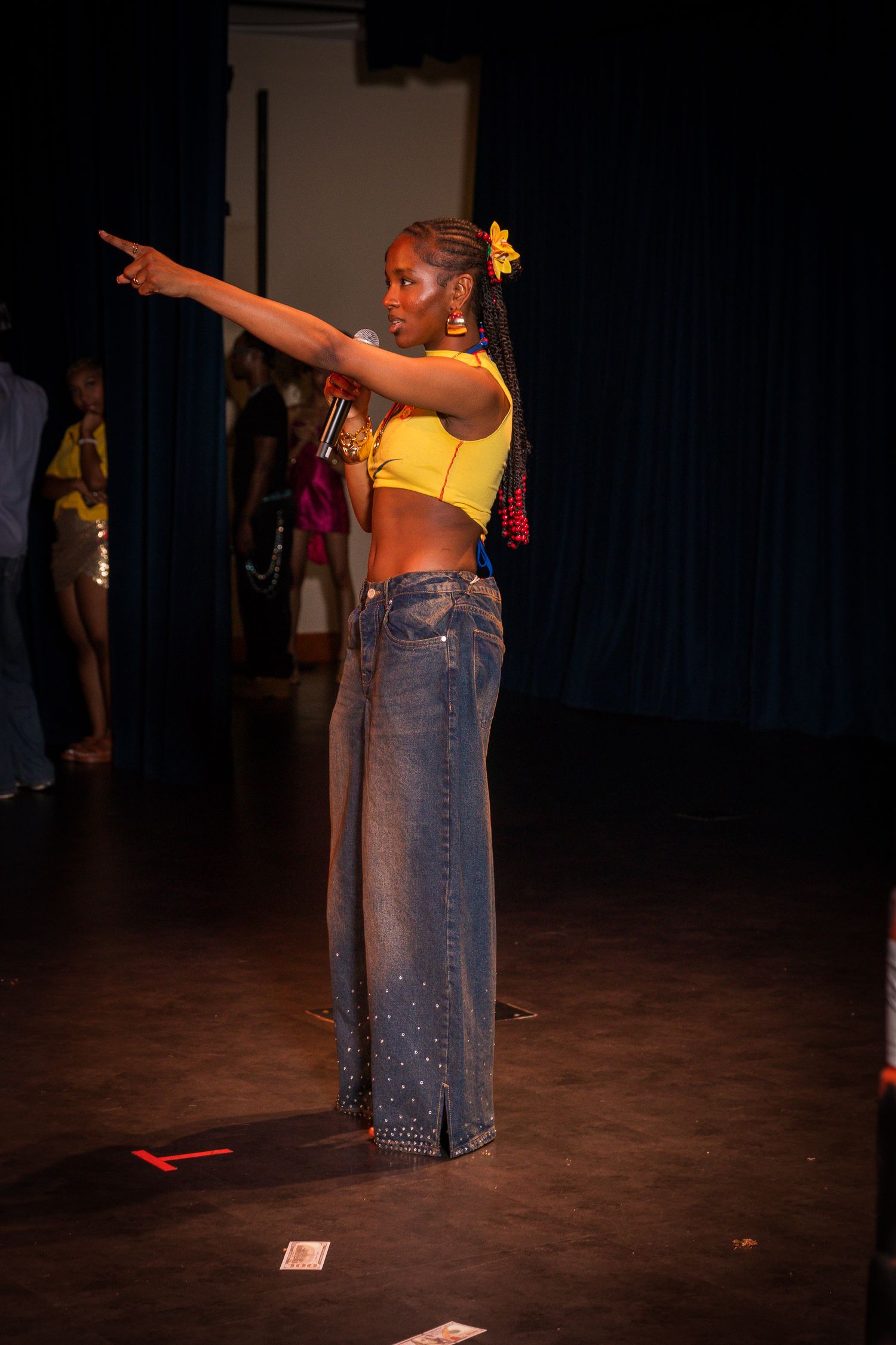 Model poses in yellow crop top and wide-leg embellished jeans with flower hair accessory on runway.