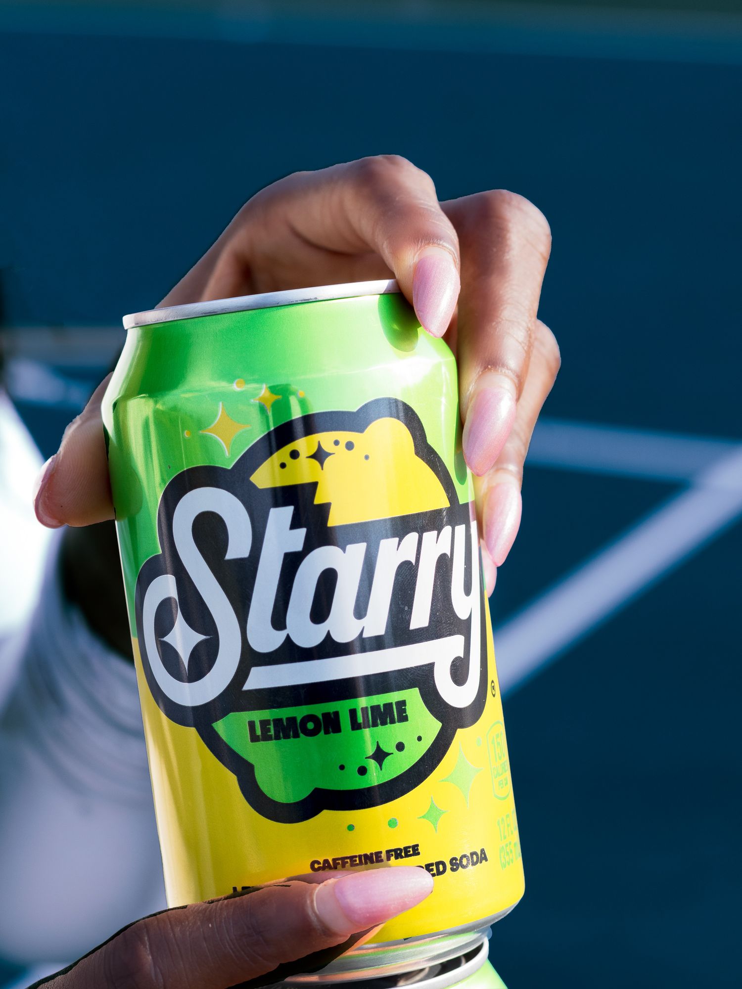 Hand holding a Starry Lemon Lime soda can on a blue tennis court background.