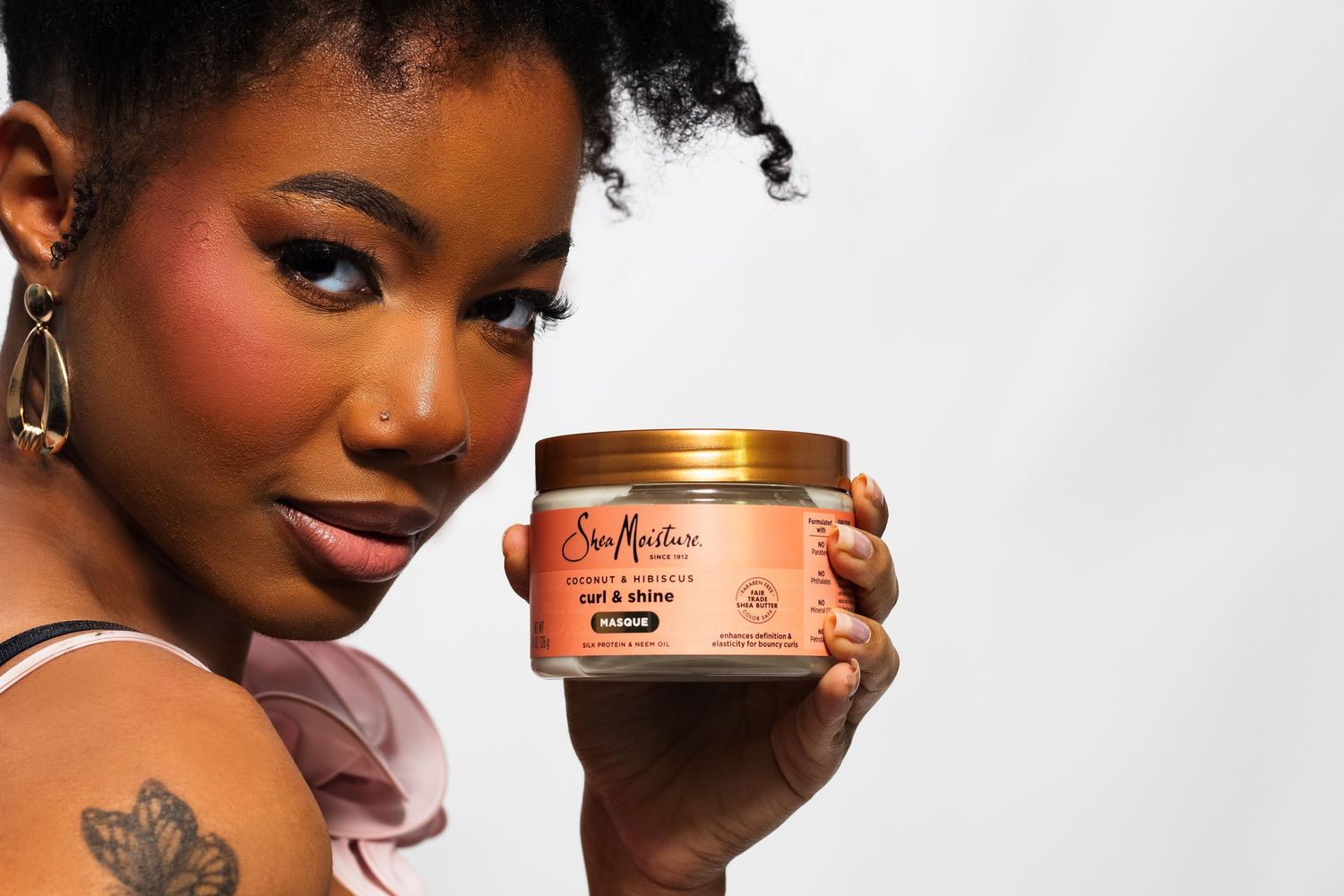 Close-up of woman with natural hair holding SheaMoisture Coconut & Hibiscus Curl & Shine mousse.