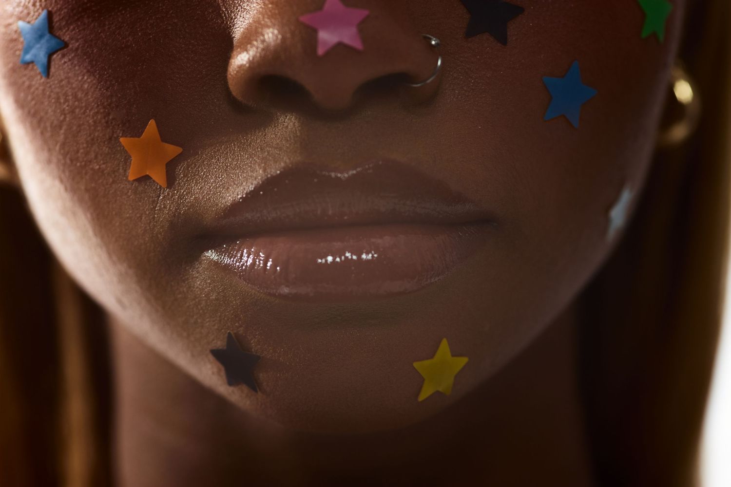 Close-up of Black woman's lips and cheeks adorned with colorful star-shaped stickers in warm lighting.