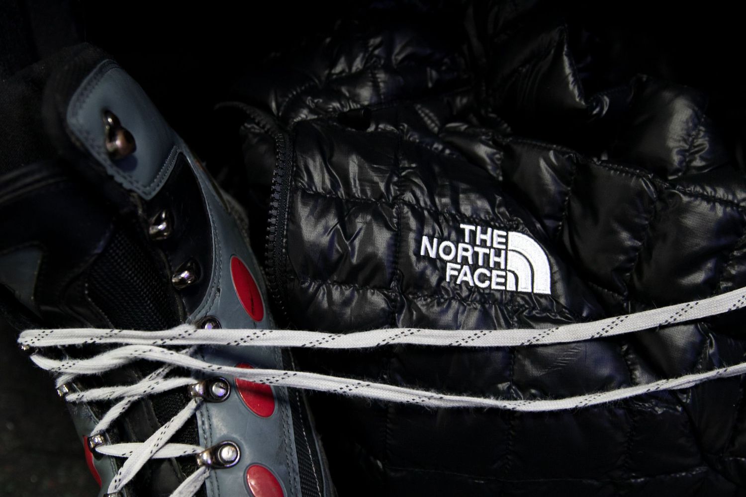 North Face black puffer jacket with rope and boots in dark setting.