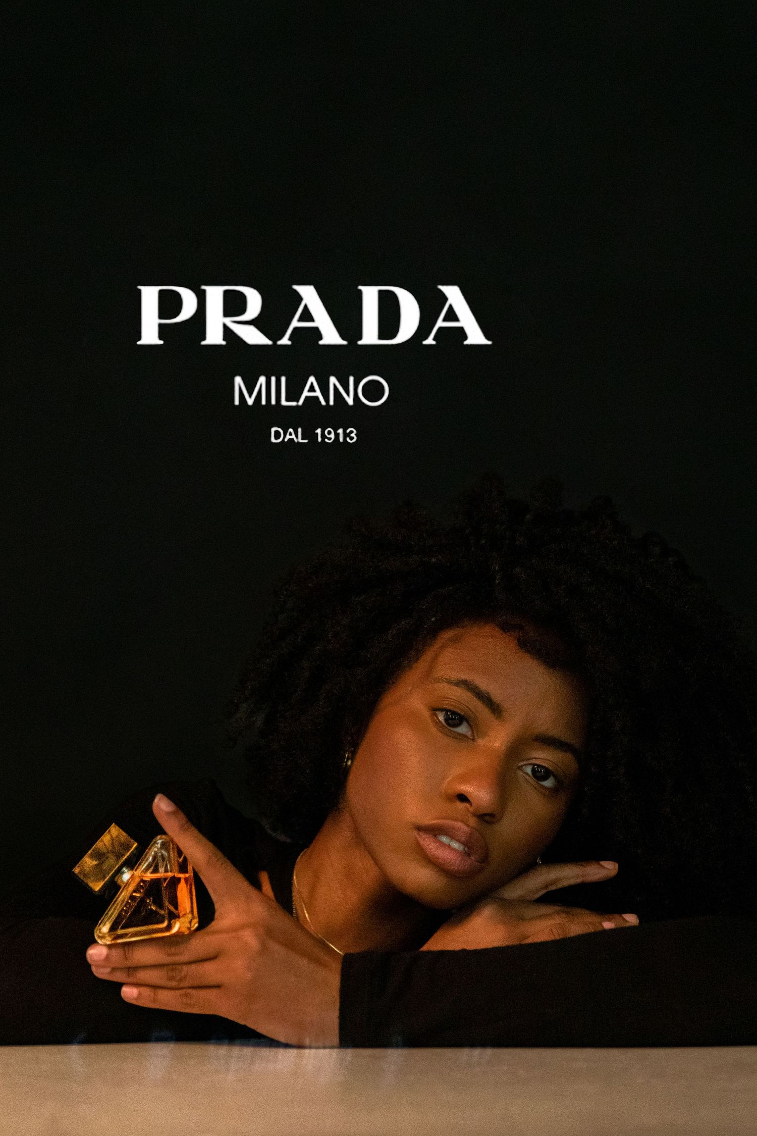 Woman posing with Prada Milano perfume bottle against dark background with brand logo overhead.