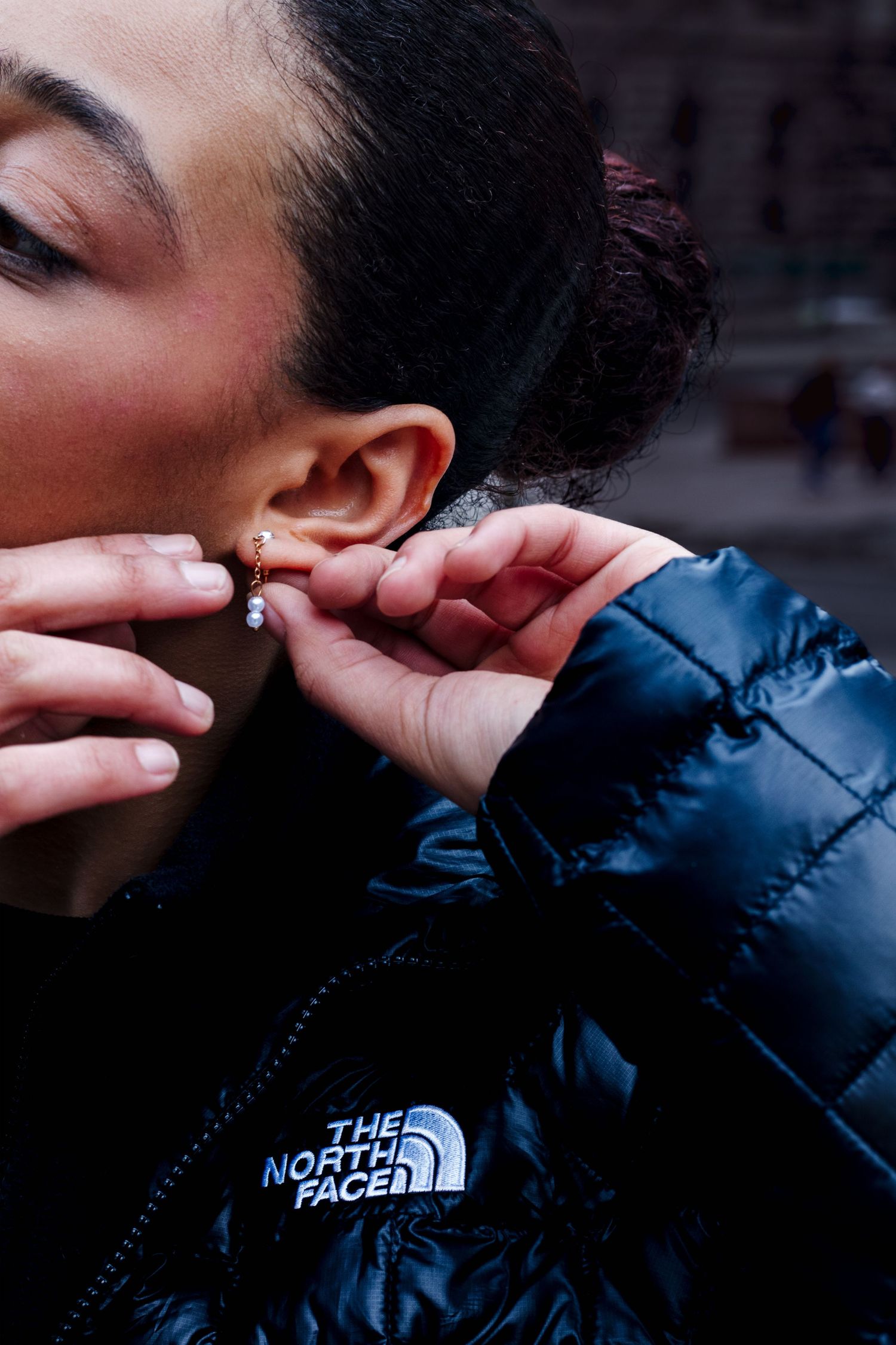 Close-up of woman adjusting gold earring wearing black North Face puffer jacket.