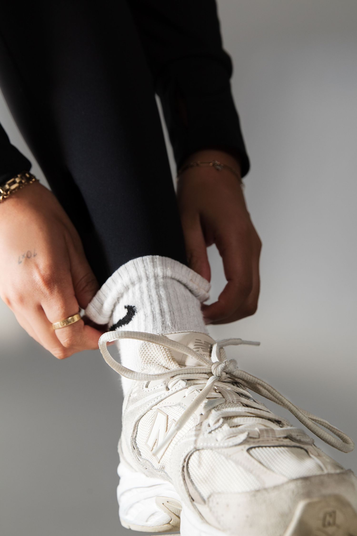 Close-up of hands adjusting white Nike socks on chunky white sneakers with gold bracelet detail.