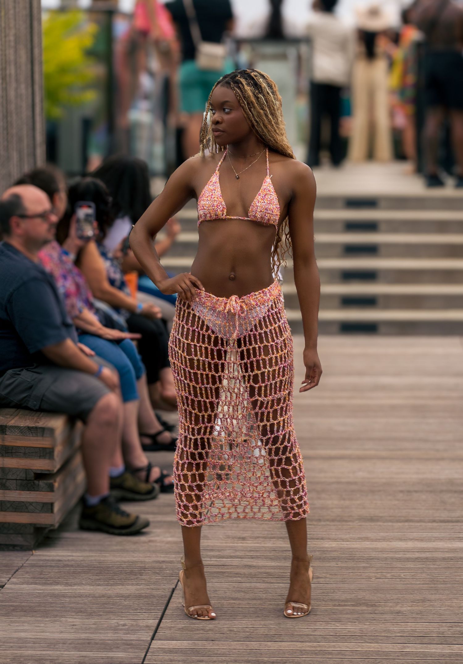 Slim model walks runway in pink crochet bikini top and sheer mesh midi skirt with heeled sandals.