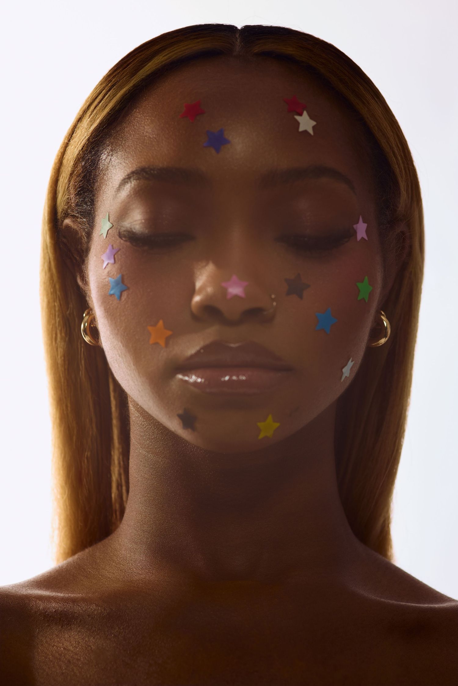 Serene Black woman with closed eyes adorned with multicolored star stickers across her face and nose ring.