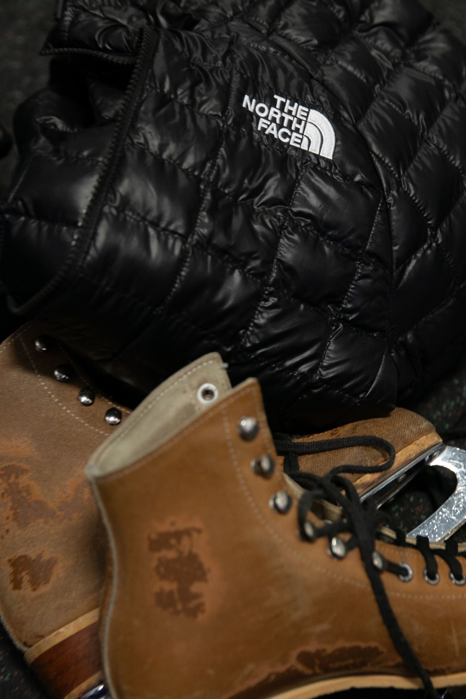 Black North Face puffer jacket beside worn tan leather lace-up boots.