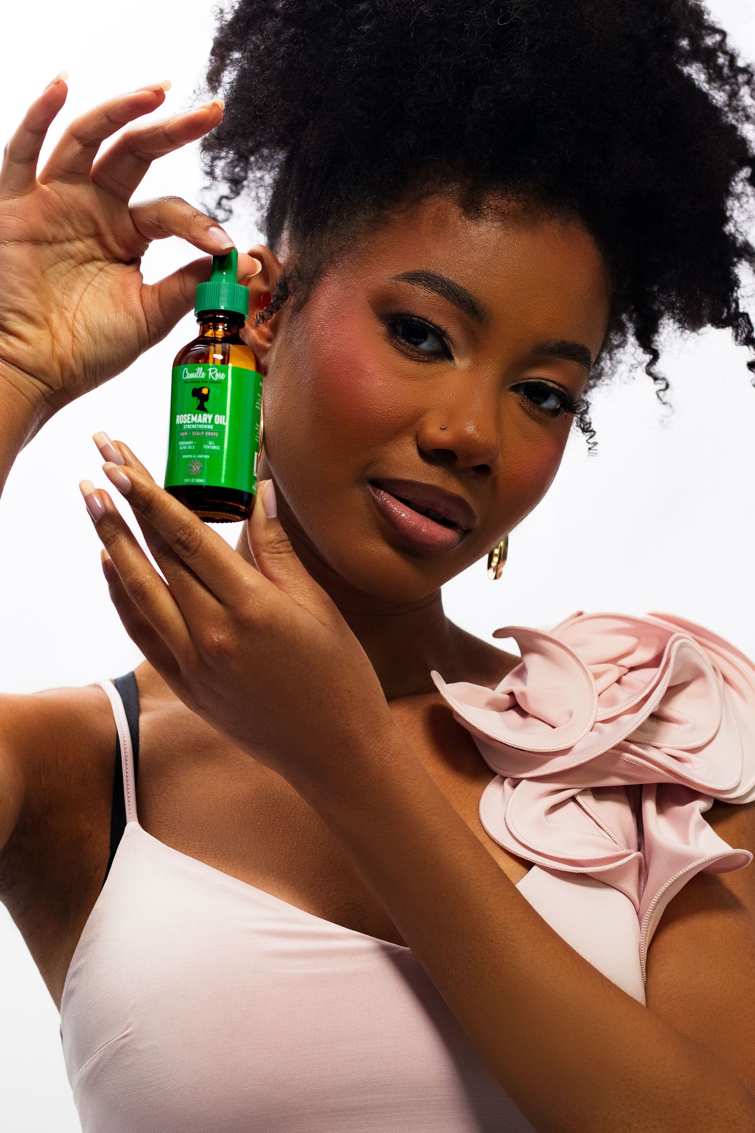 Woman with natural afro holding small green herbal oil dropper bottle near her face.
