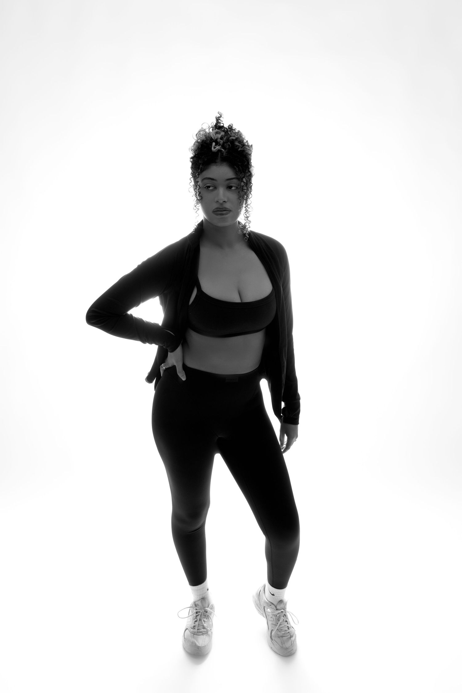 Black and white photo of a woman in athletic wear posing confidently against a bright background.