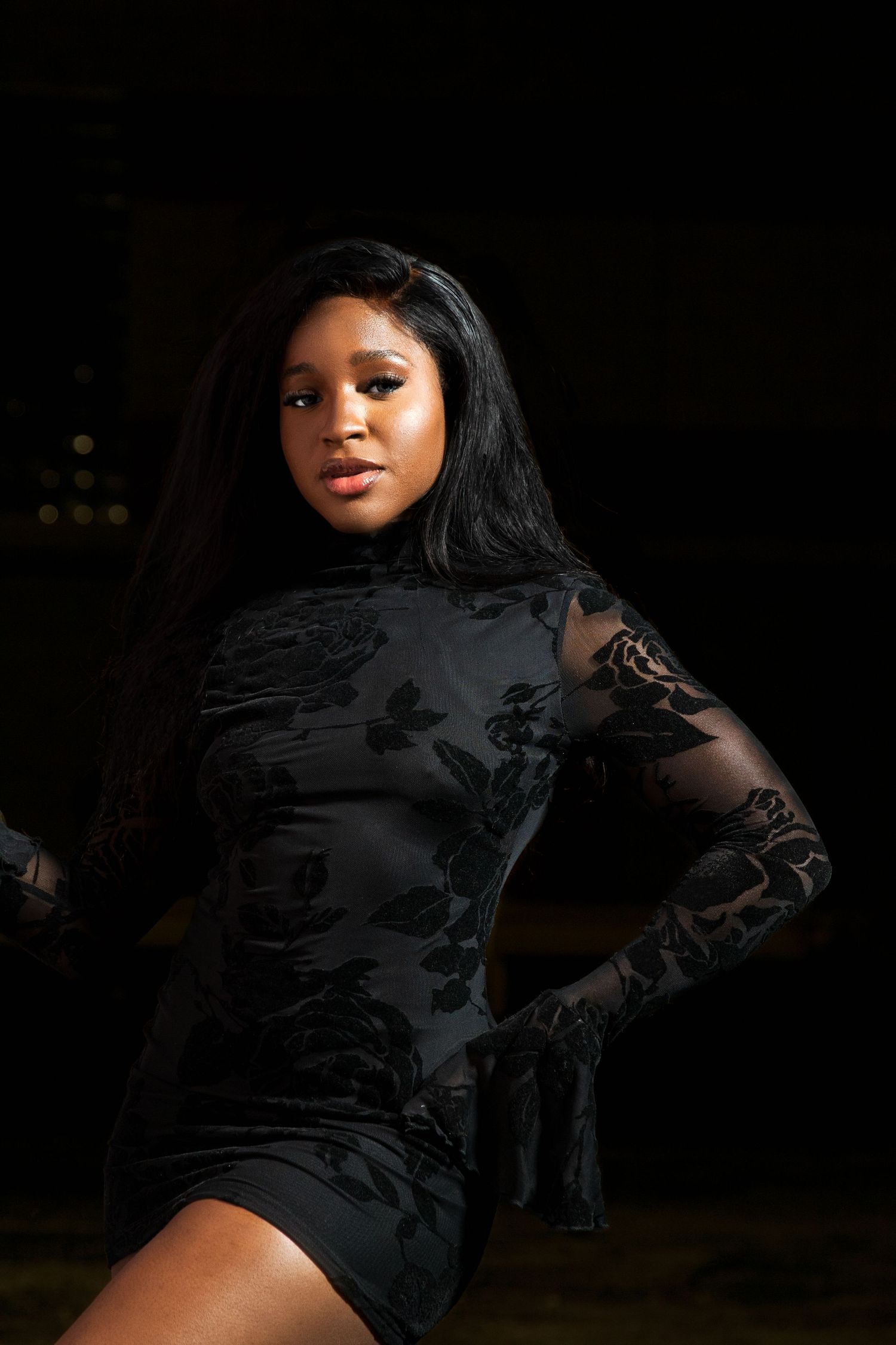 Woman in black floral velvet mini dress poses in dramatic lighting.