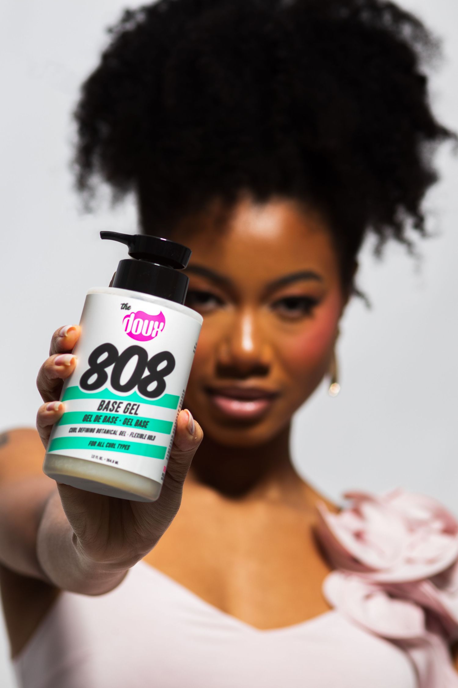 Woman with natural afro extending The Doux 808 Base Gel jar toward camera in focus.
